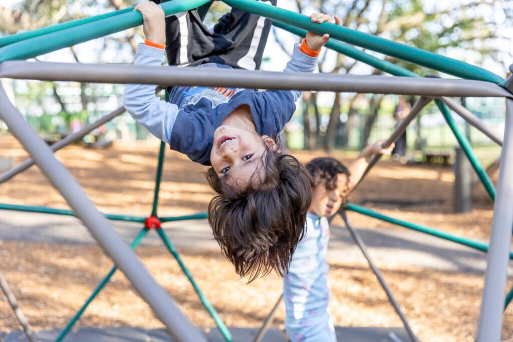 Two preschool children laughing while playing on a dome climber at the Preschool for Creative Learning